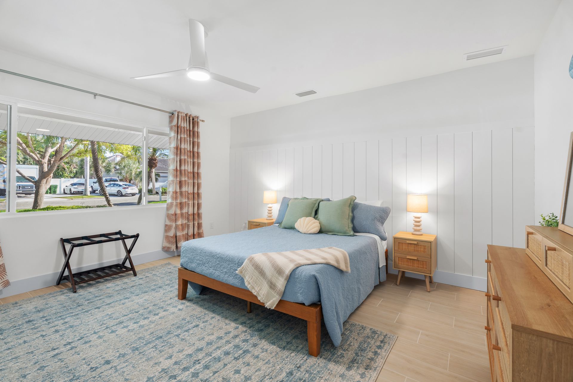 Bright bedroom with blue bedspread, patterned rug, and ocean-view sliding doors