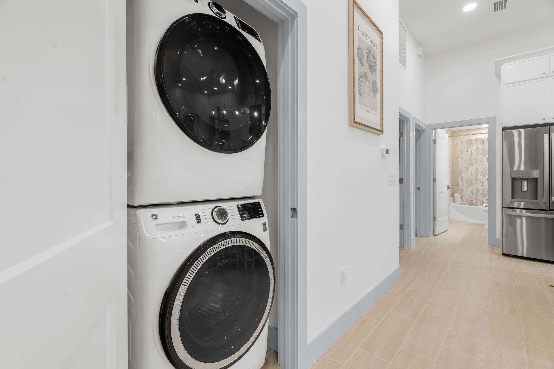 Stacked washer and dryer in a narrow hallway beside a bright kitchen area