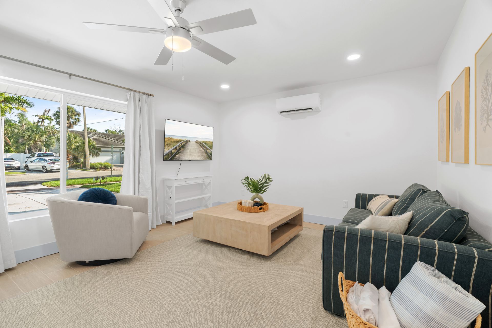 Bright living room with white walls, beige carpet, striped sofa, armchair, coffee table, and large windows.