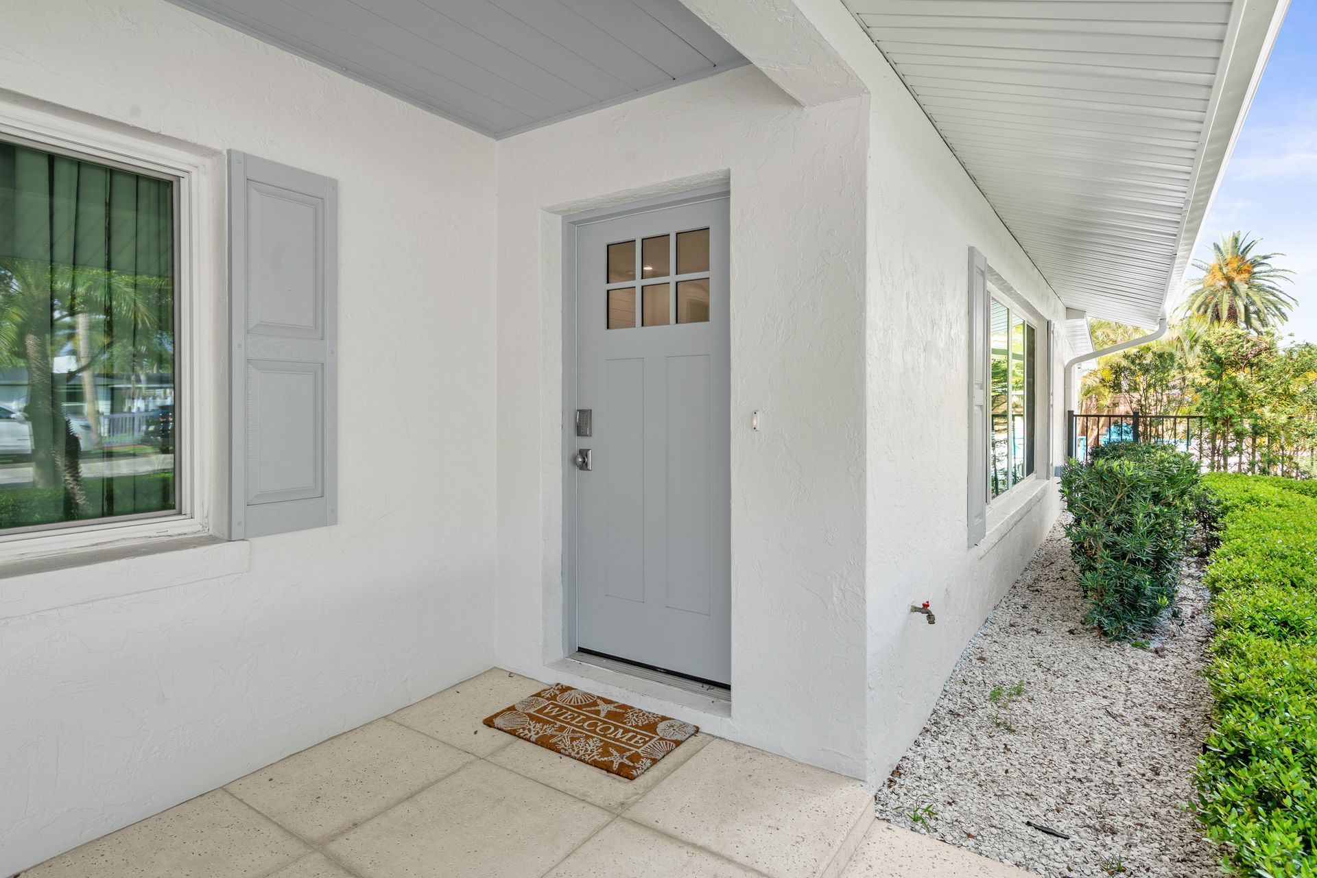 White front entry with a gray door, shuttered window, and gravel walkway beside a house