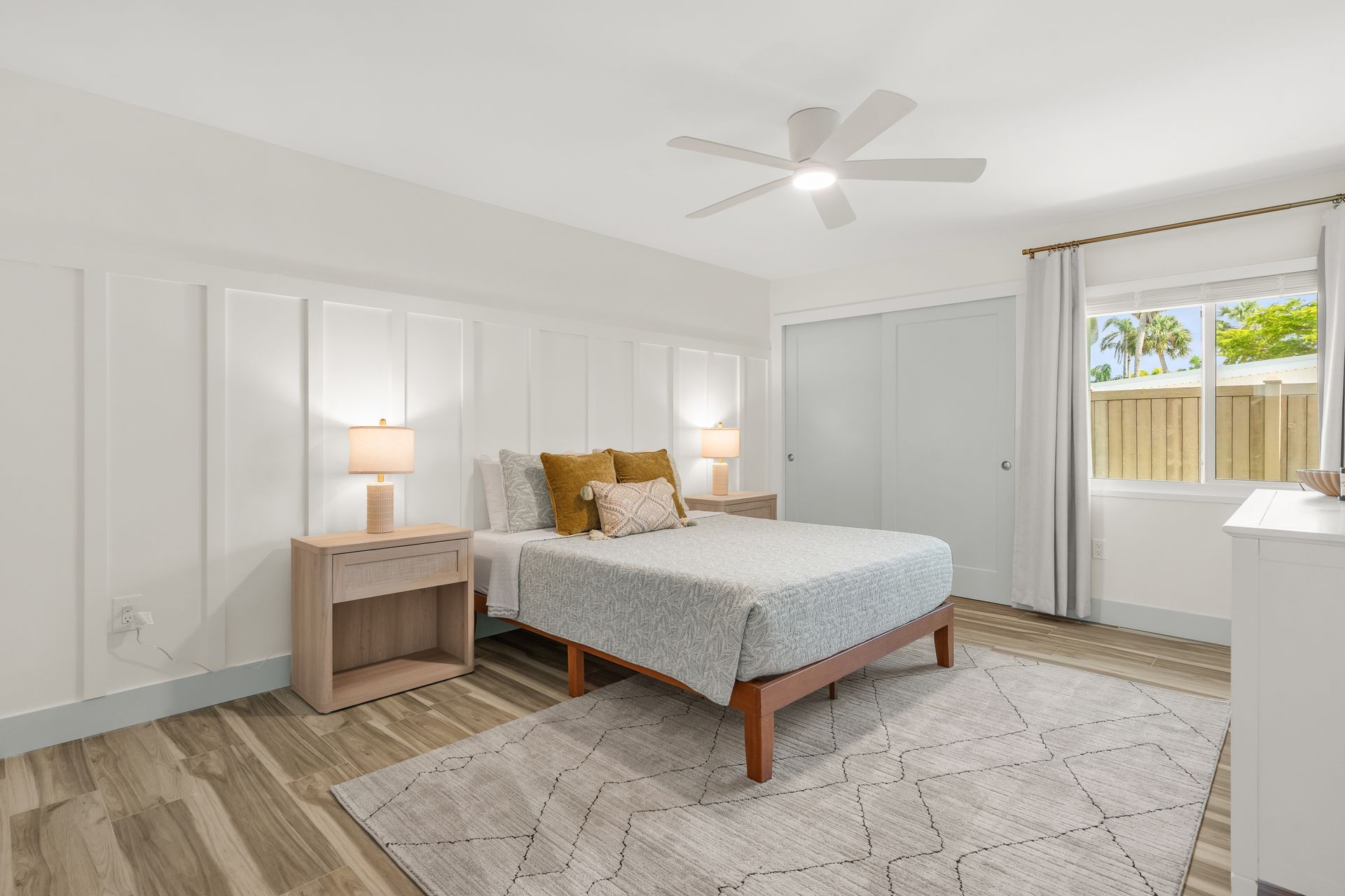 Bright bedroom with a bed, nightstand lamp, ceiling fan, closet, and window with curtains