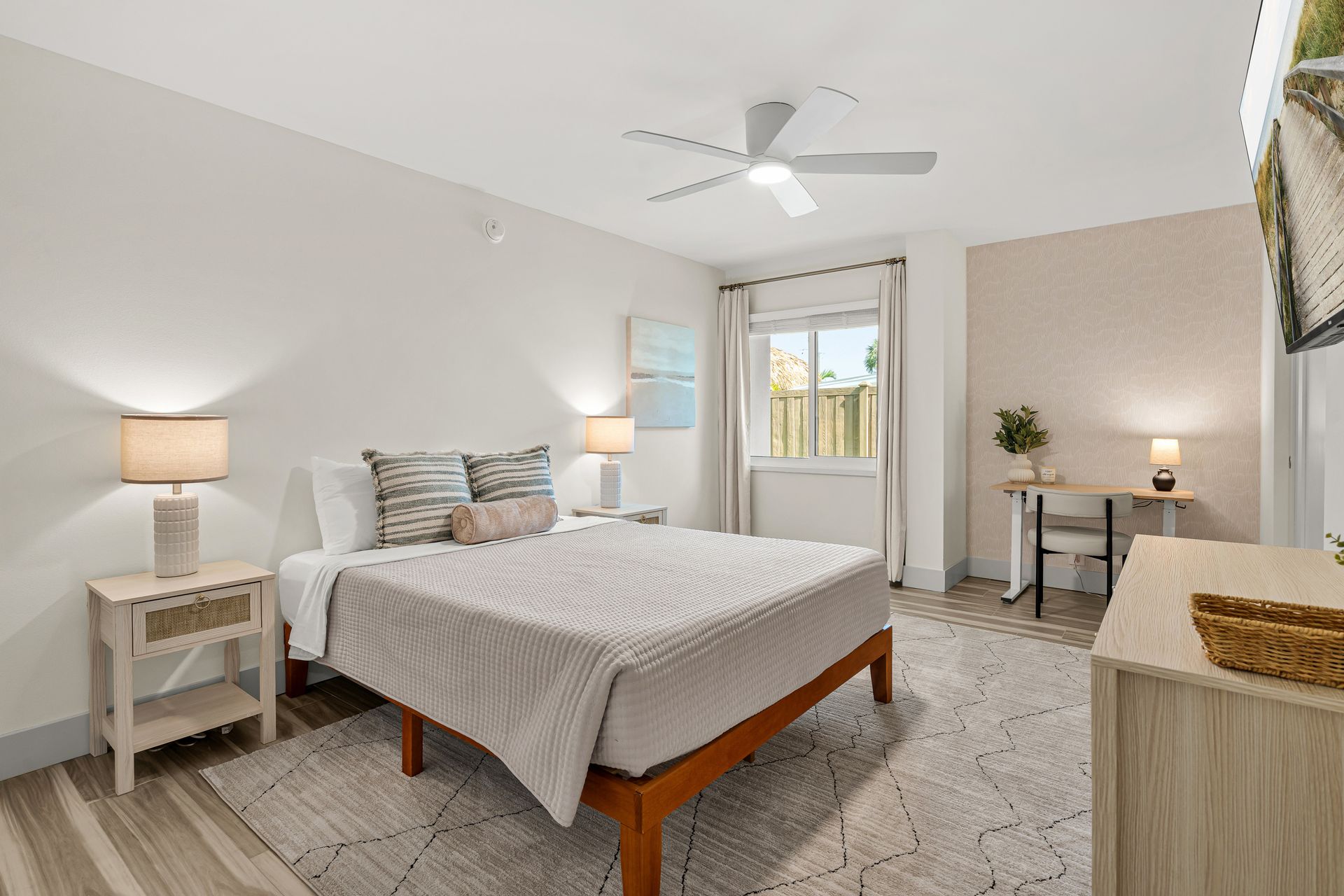 Bright bedroom with a bed, nightstands, ceiling fan, and a small desk by a window