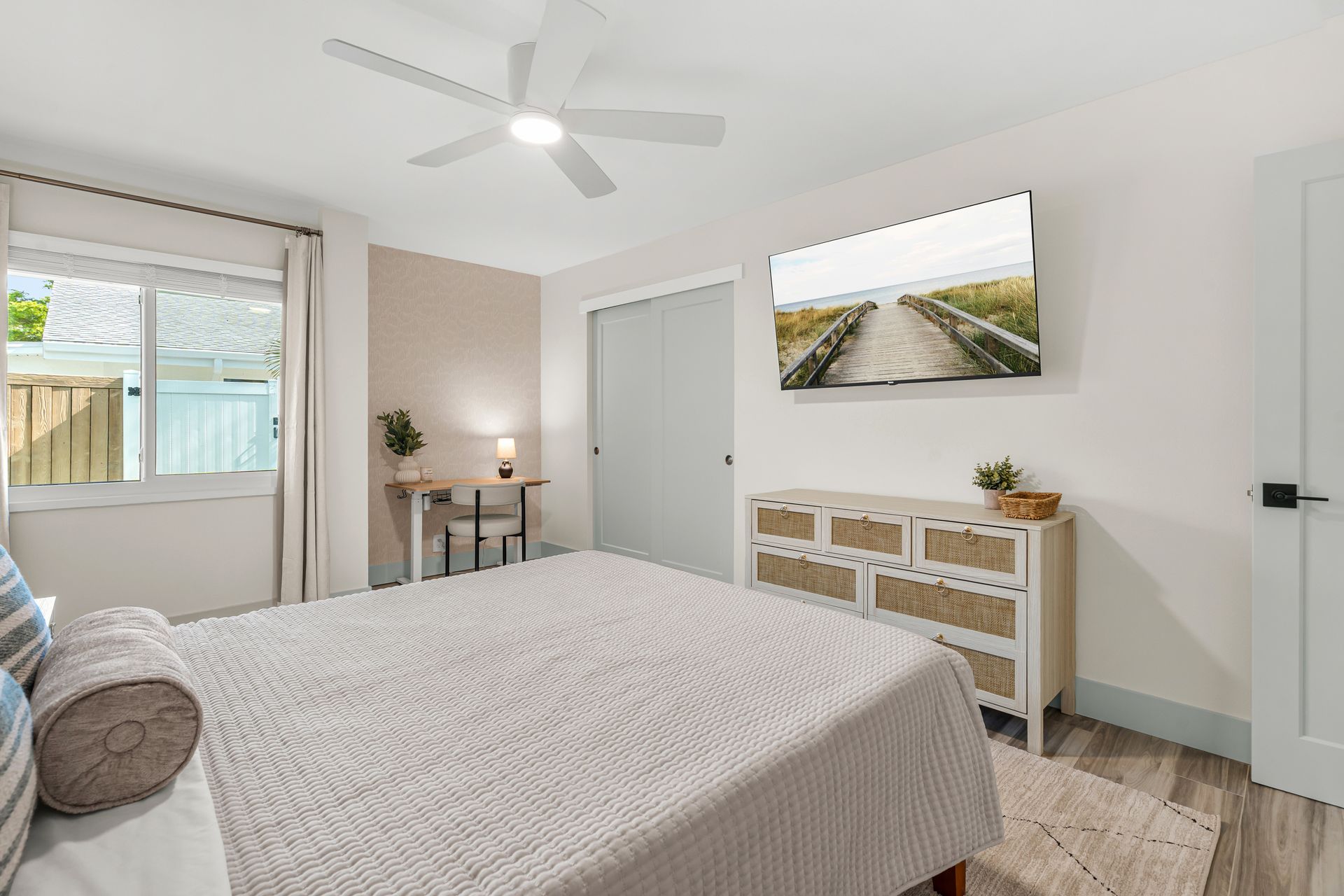 Bright bedroom with a bed, dresser, desk, ceiling fan, and window with curtains