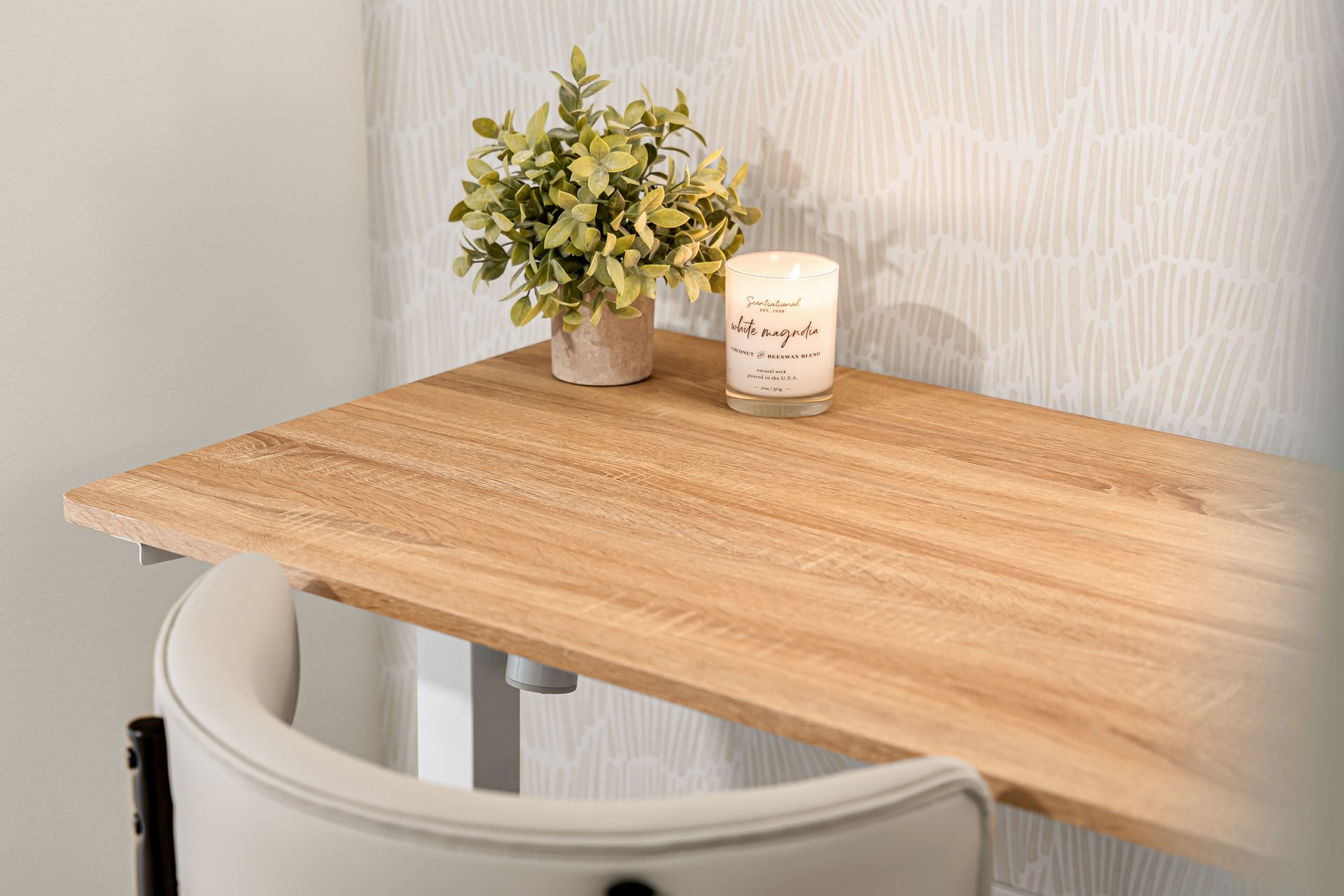 Small wooden table with a potted plant and candle beside a white chair near a wall.