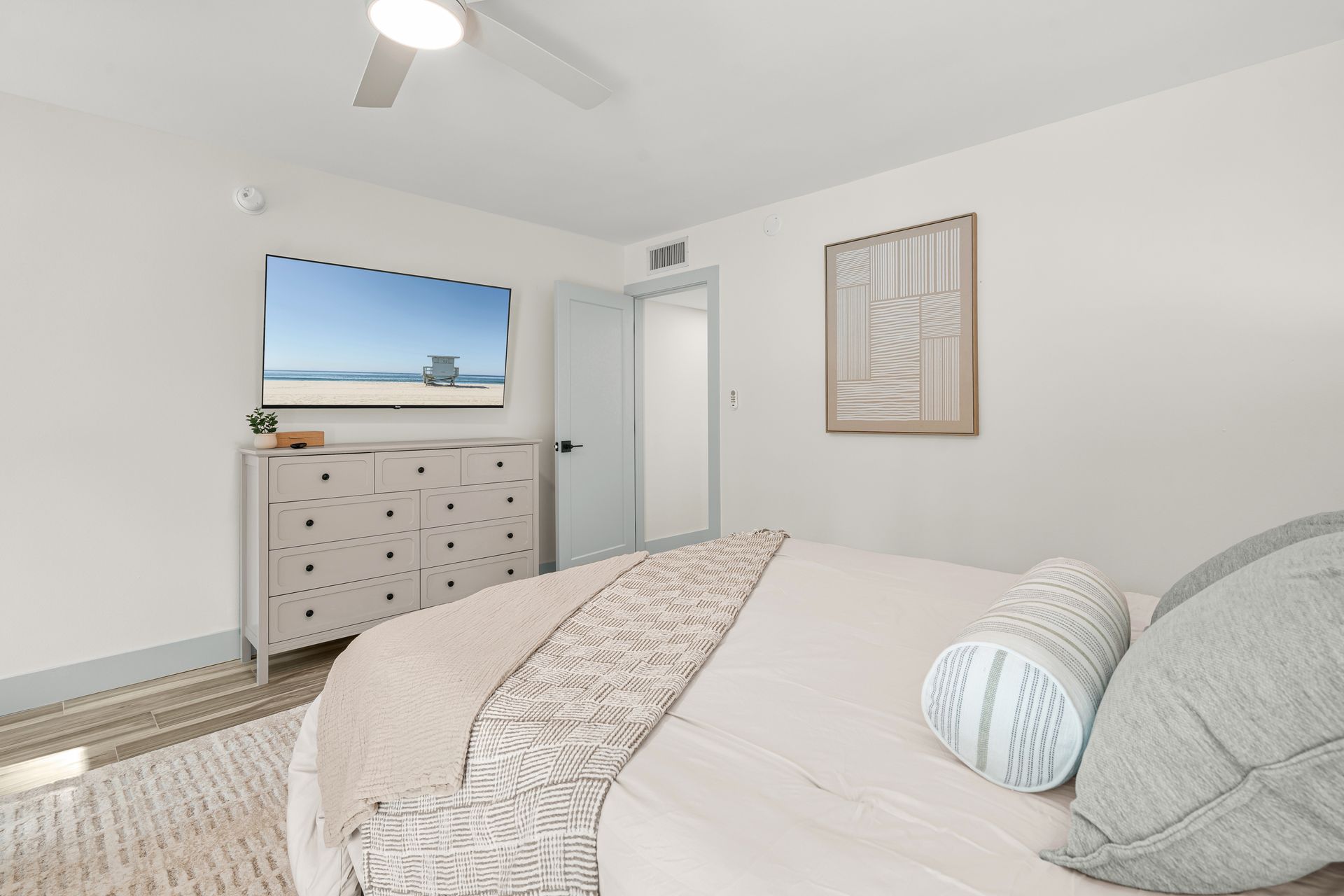 Bright bedroom with a bed, dresser, wall art, and ceiling fan in white decor