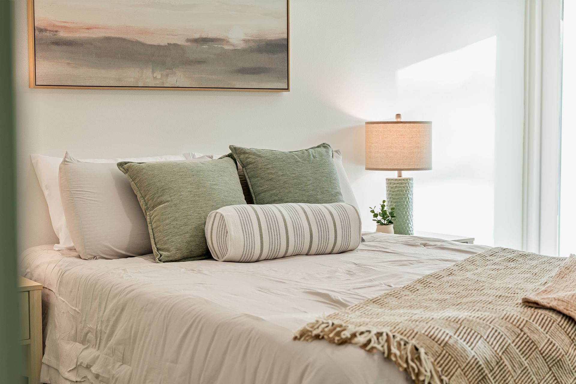 Bright bedroom with a white bed, green pillows, textured throw, and a bedside lamp