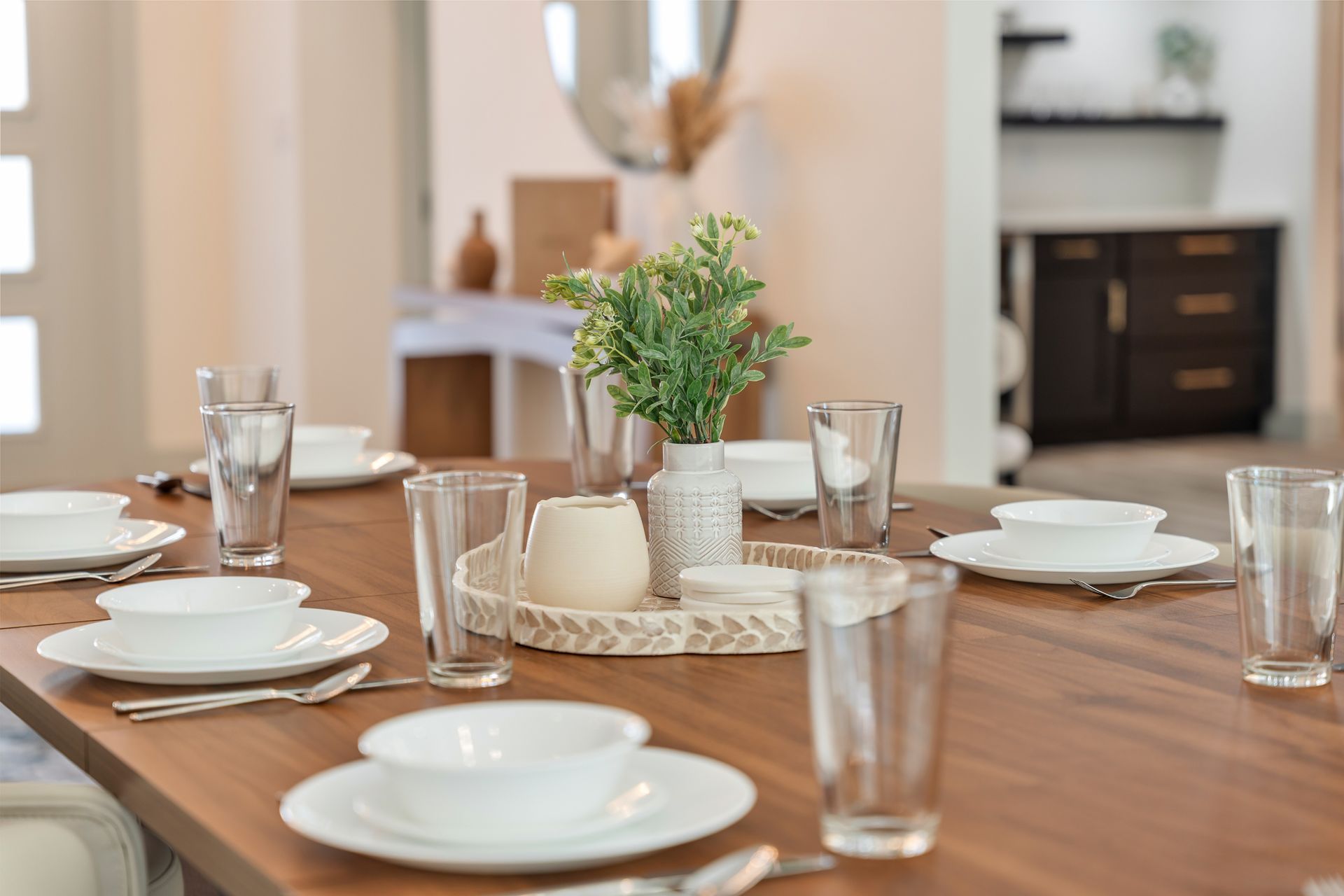 Dining table set with white plates, glasses, candles, and a small potted plant centerpiece