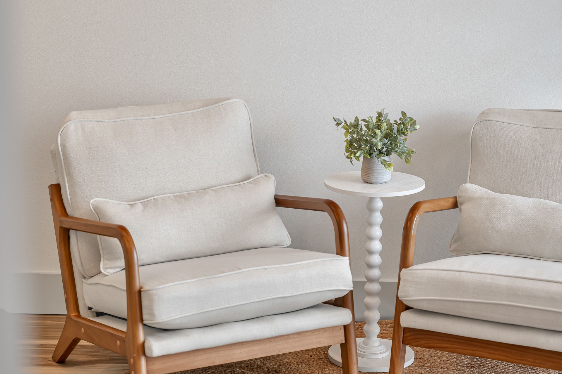 Two white armchairs with wood arms beside a small round table holding a vase of flowers