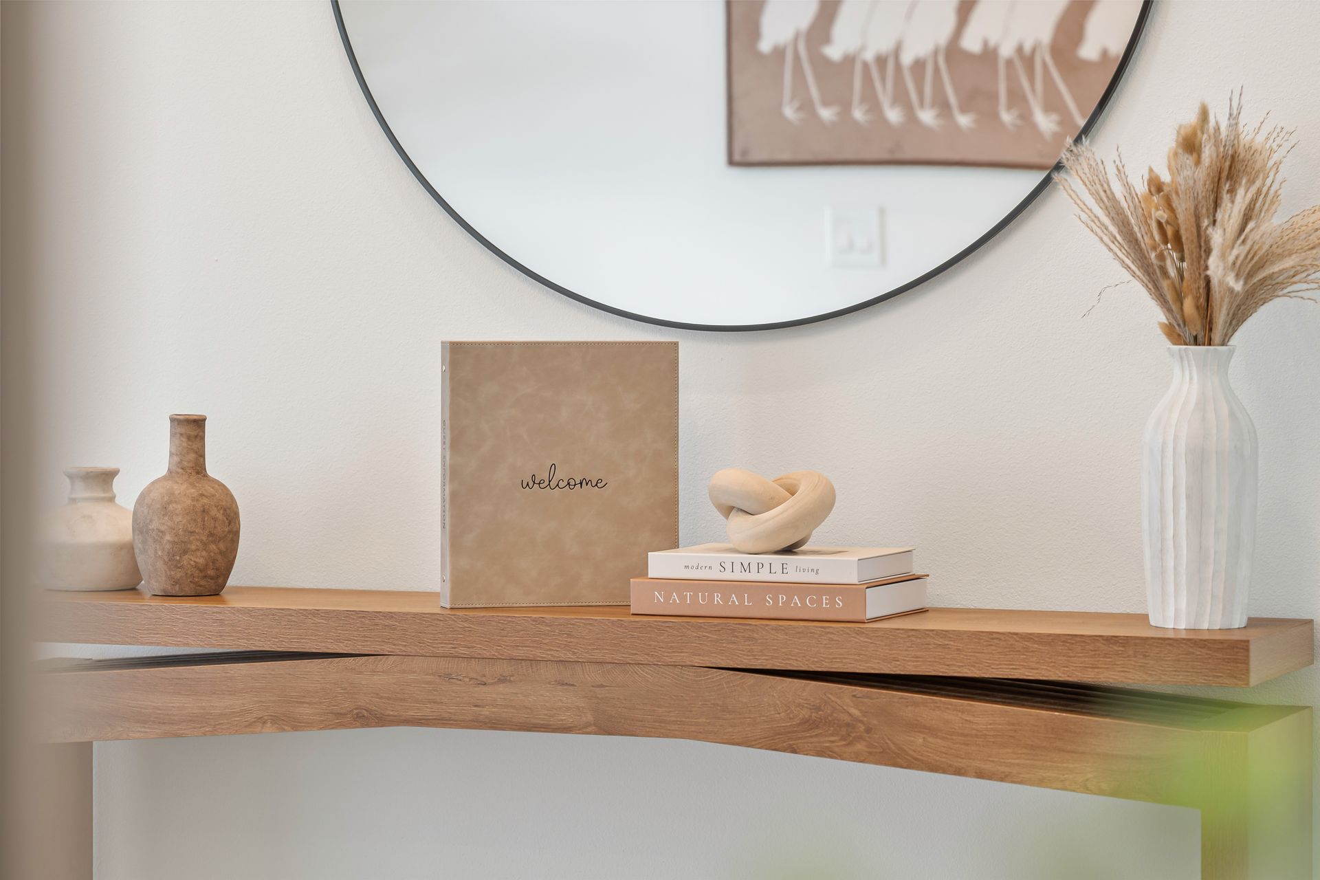 Minimalist console table with vase, books, bowl, dried grass, and round mirror