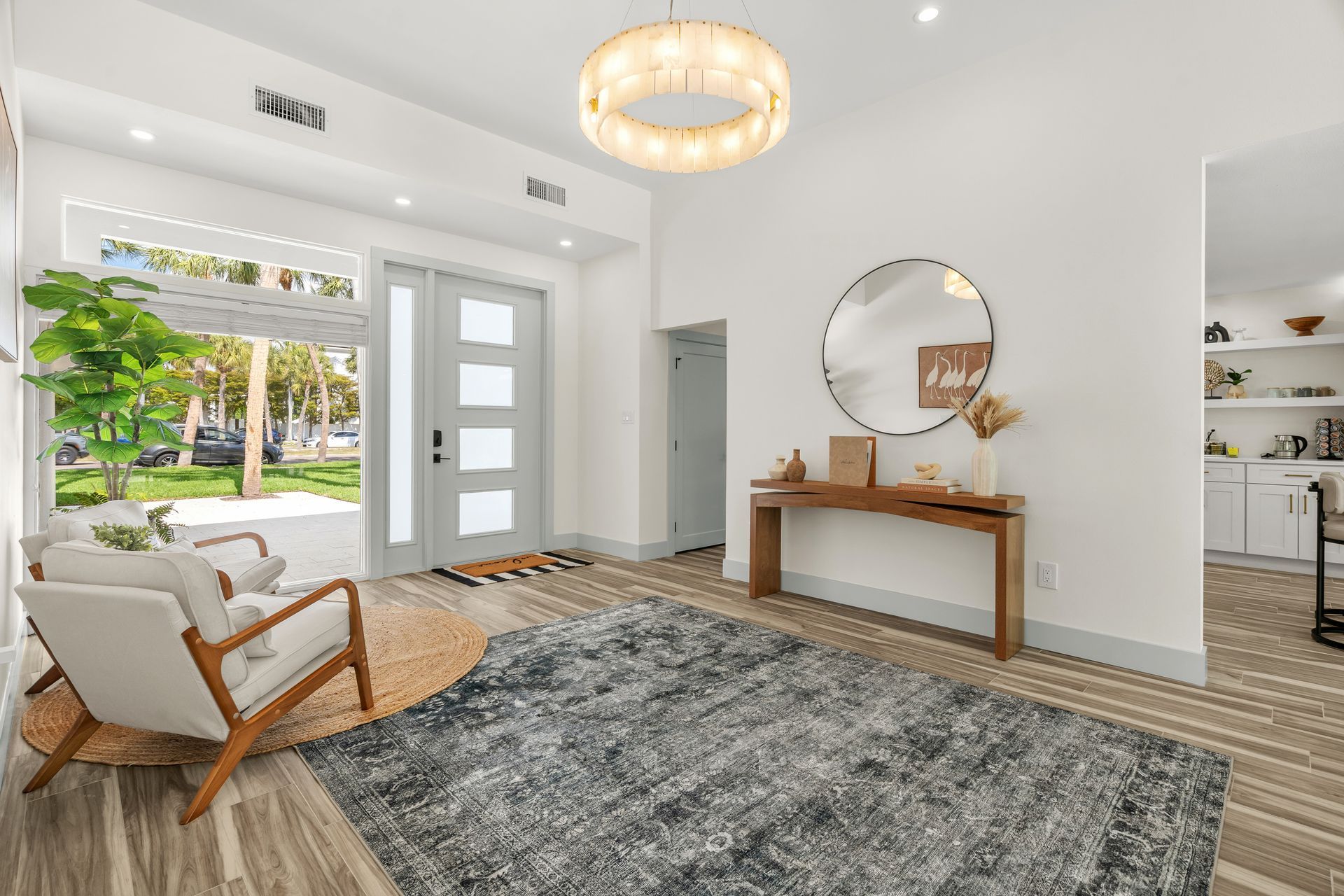 Bright modern entryway with white walls, gray rug, console table, round mirror, and natural light.