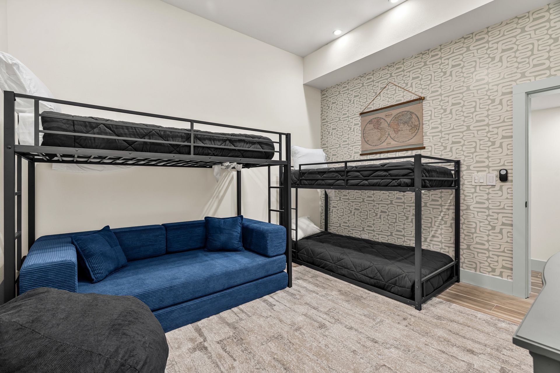 Small bedroom with two black bunk beds and a blue couch against a white wall.
