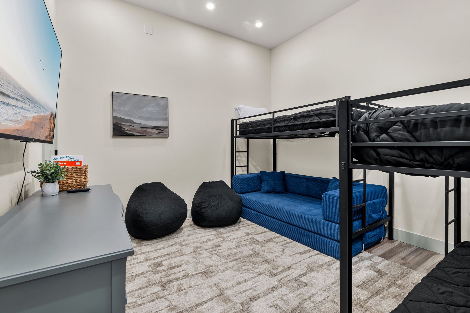 Shared bedroom with bunk beds, blue couch, two black beanbags, and a desk in a bright room