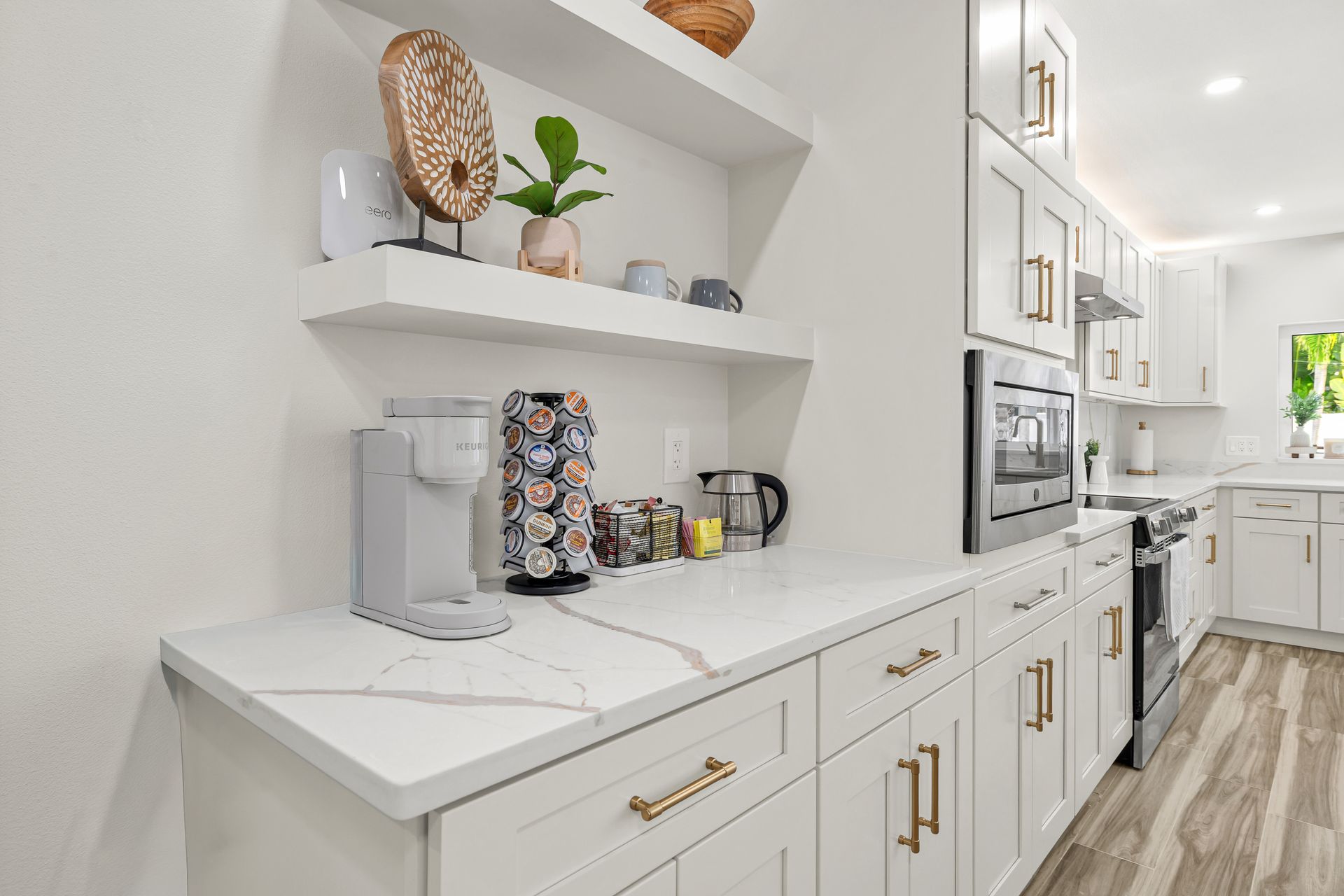 Bright white kitchen coffee station with floating shelves, coffee maker, mugs, and gold hardware