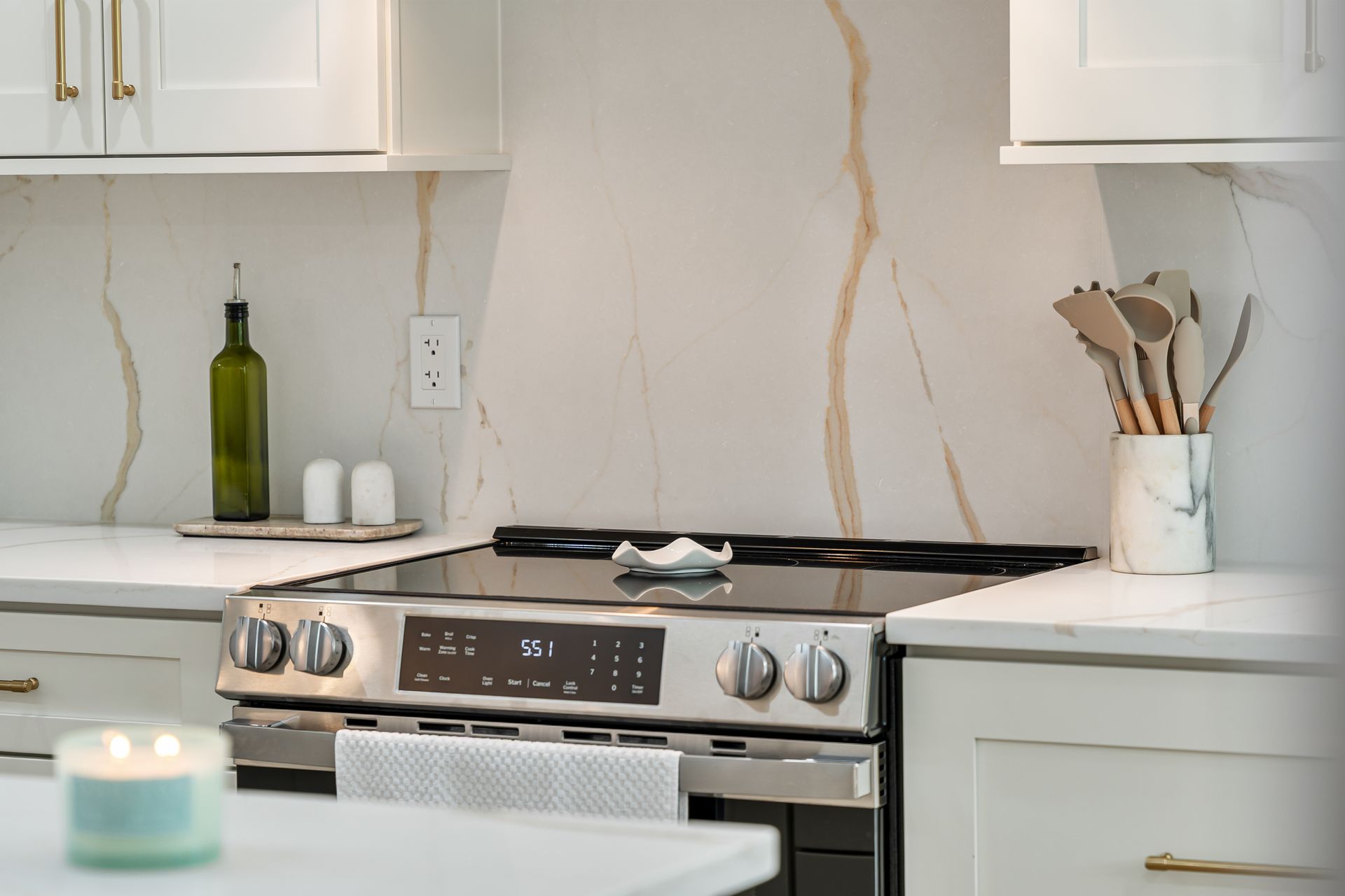 Modern kitchen with white cabinets, stainless steel stove, and a candle on a white island