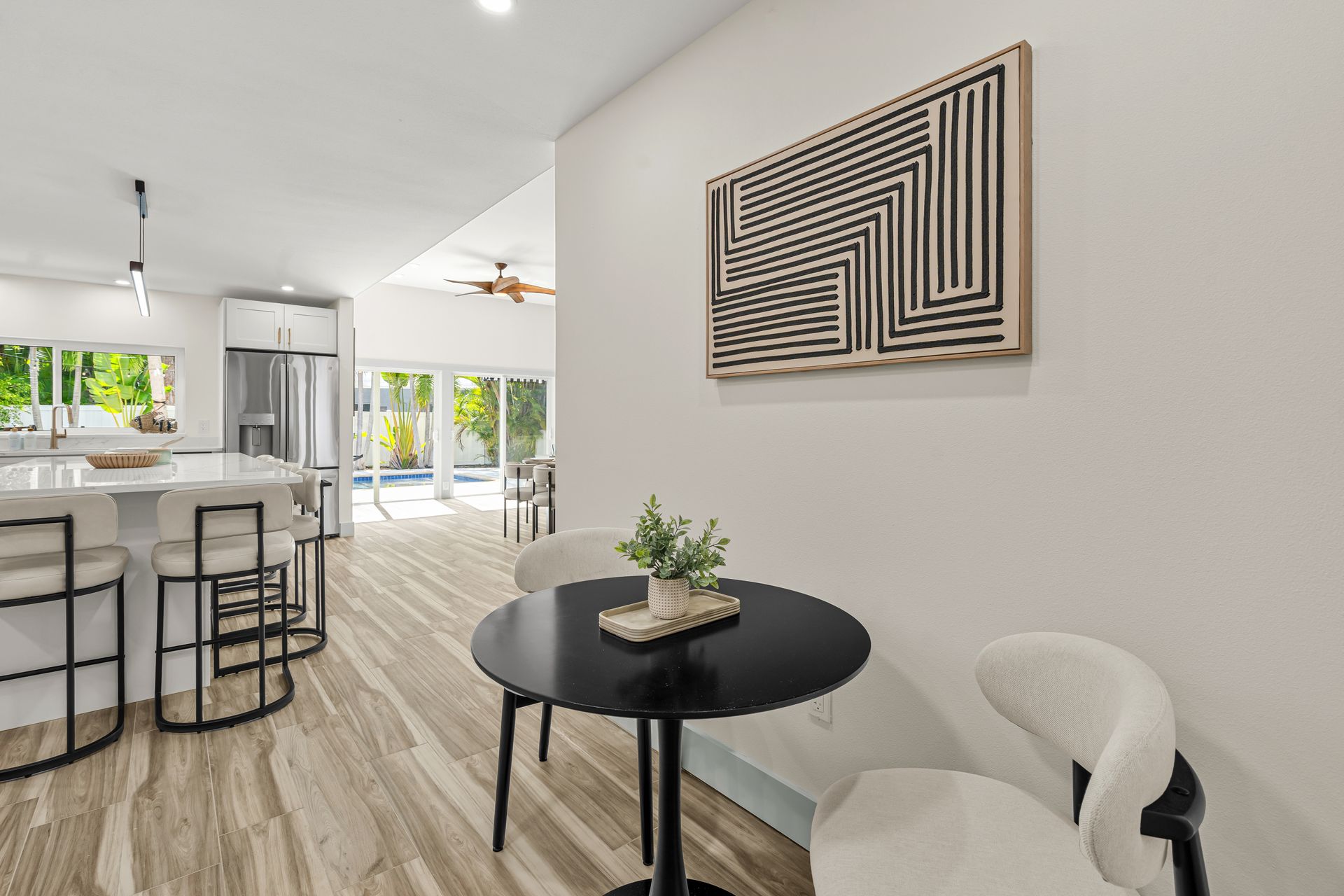 Modern open-plan living room with white chairs, black table, and geometric wall art.