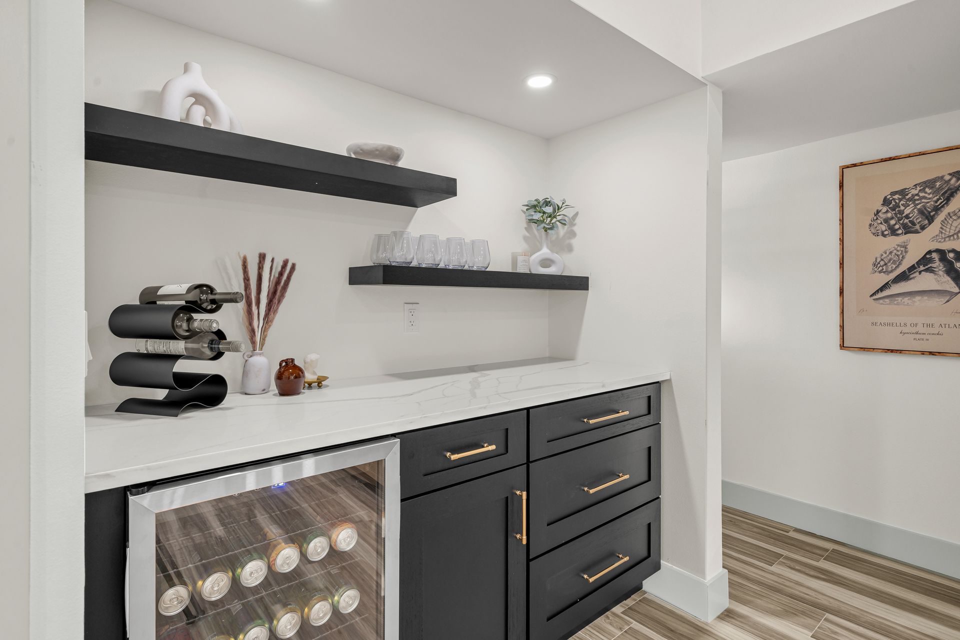 Modern wine bar with dark cabinets, white countertop, floating shelves, and decorative accents