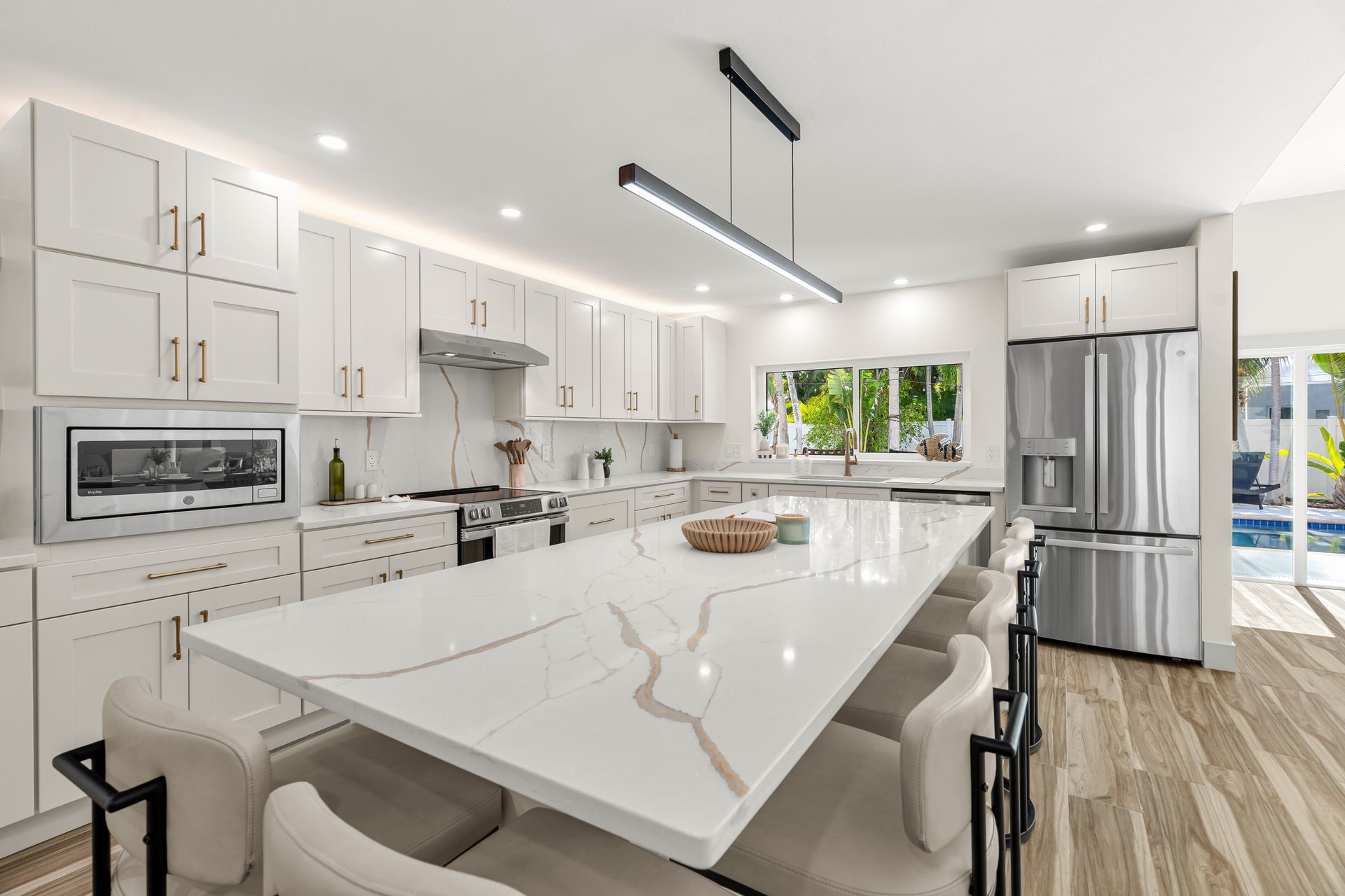 Bright modern white kitchen with island, stainless fridge, and large windows