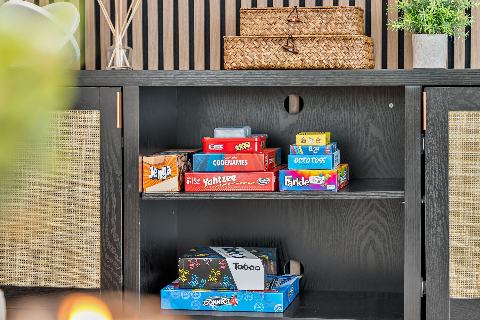 Colorful board game boxes on a dark shelf, with a woven basket on top and a woven basket at left.