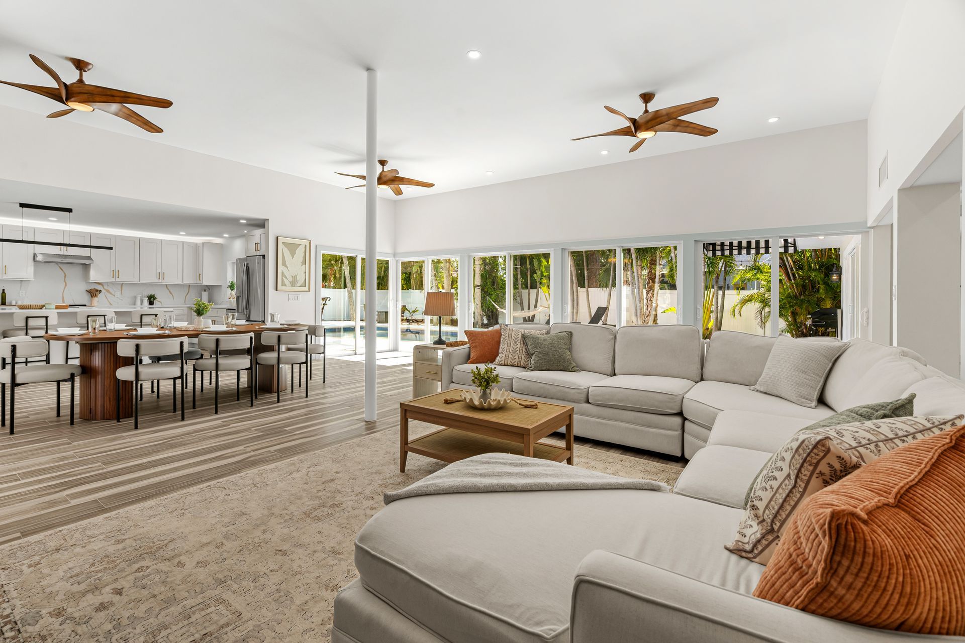 Bright open living room with white sectional sofas, beige rug, wood coffee table, and large windows to patio