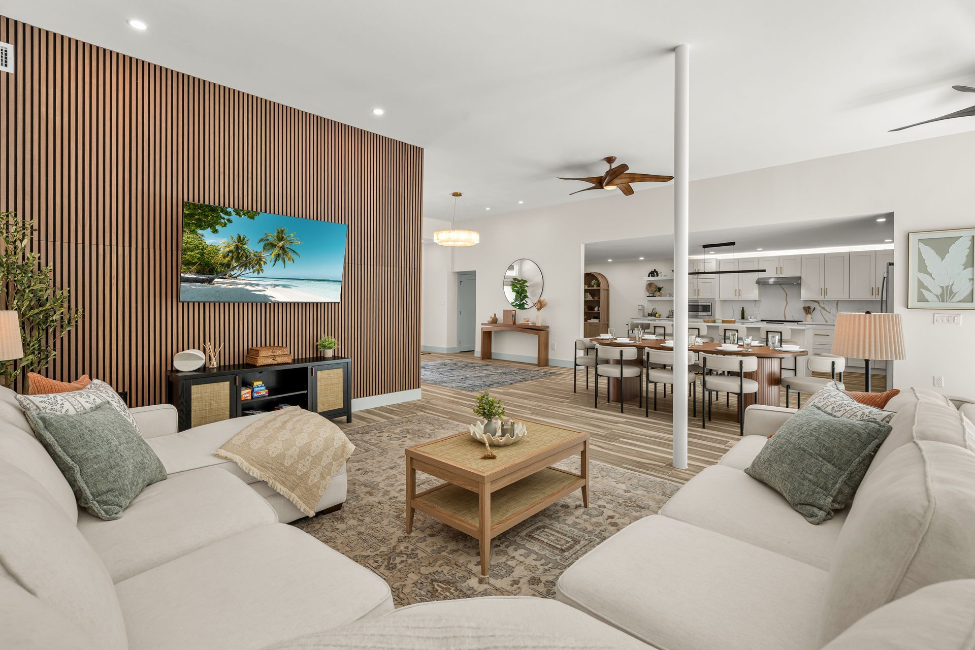 Bright open living room with beige sectional, wood accent wall, TV, and adjacent dining and kitchen area