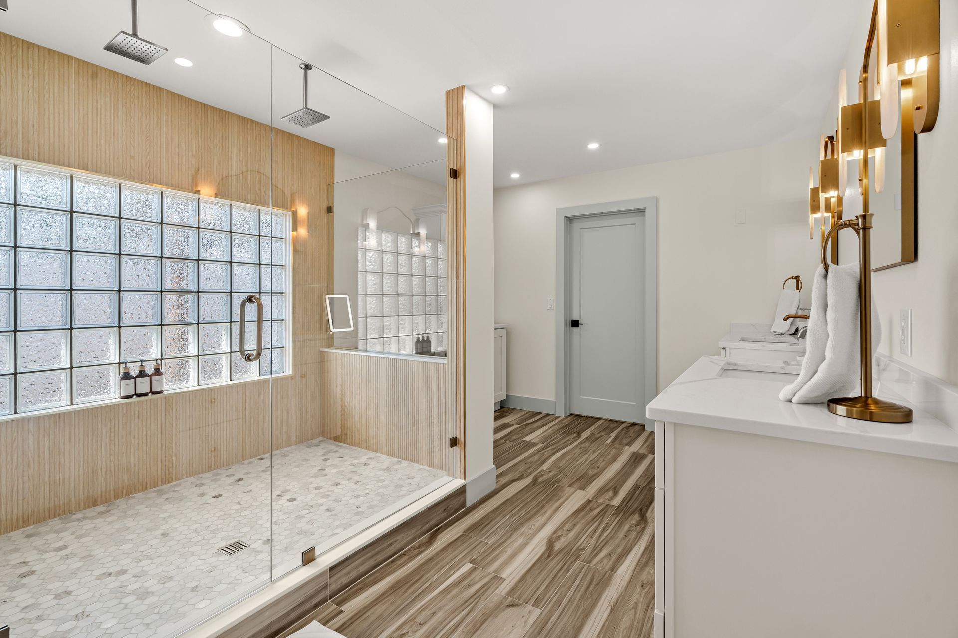 Bright modern bathroom with double vanity, walk-in shower, and freestanding tub with gold fixtures