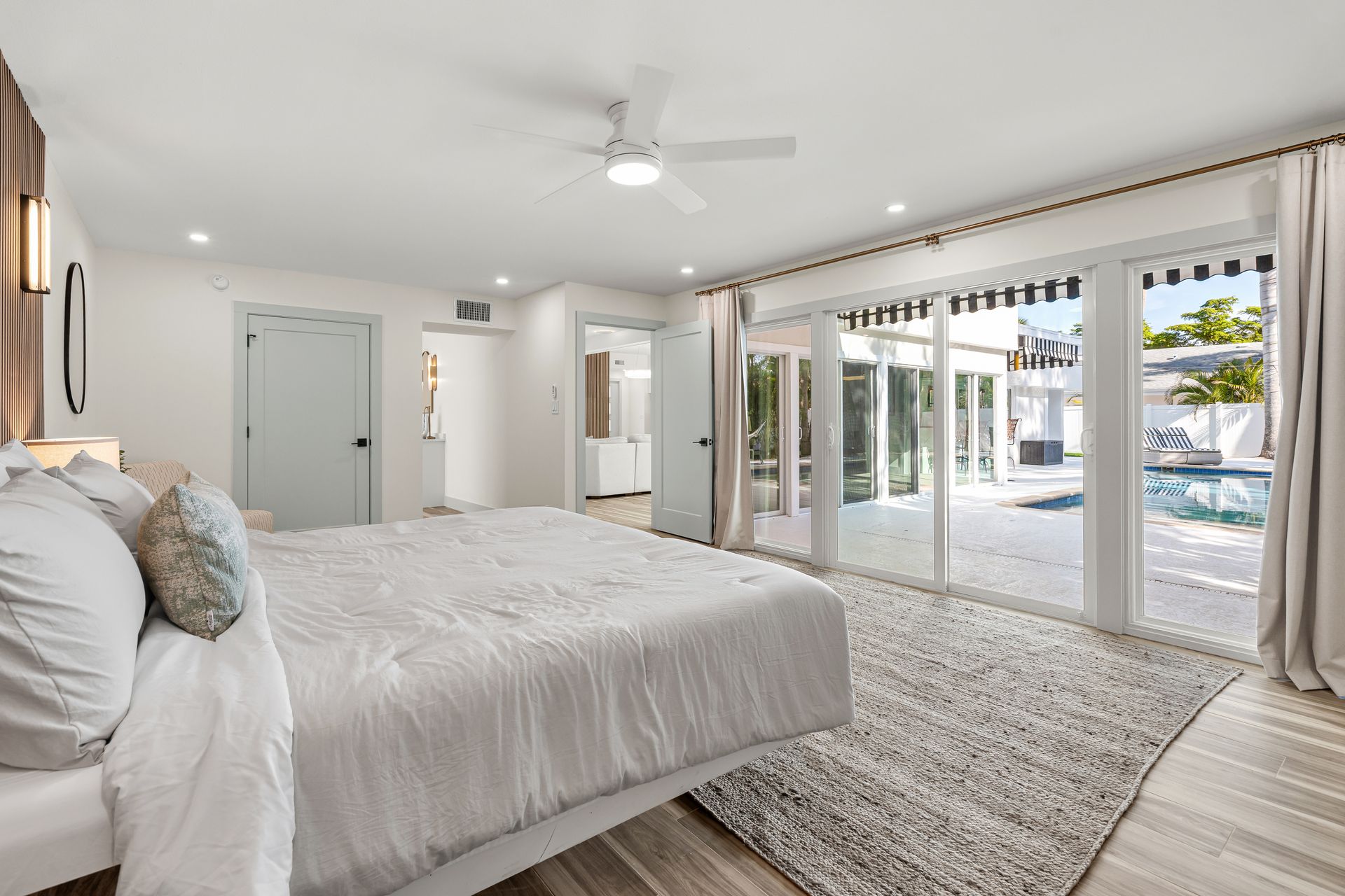 Bright bedroom with a white bed, ceiling fan, and sliding glass doors to a patio and pool area