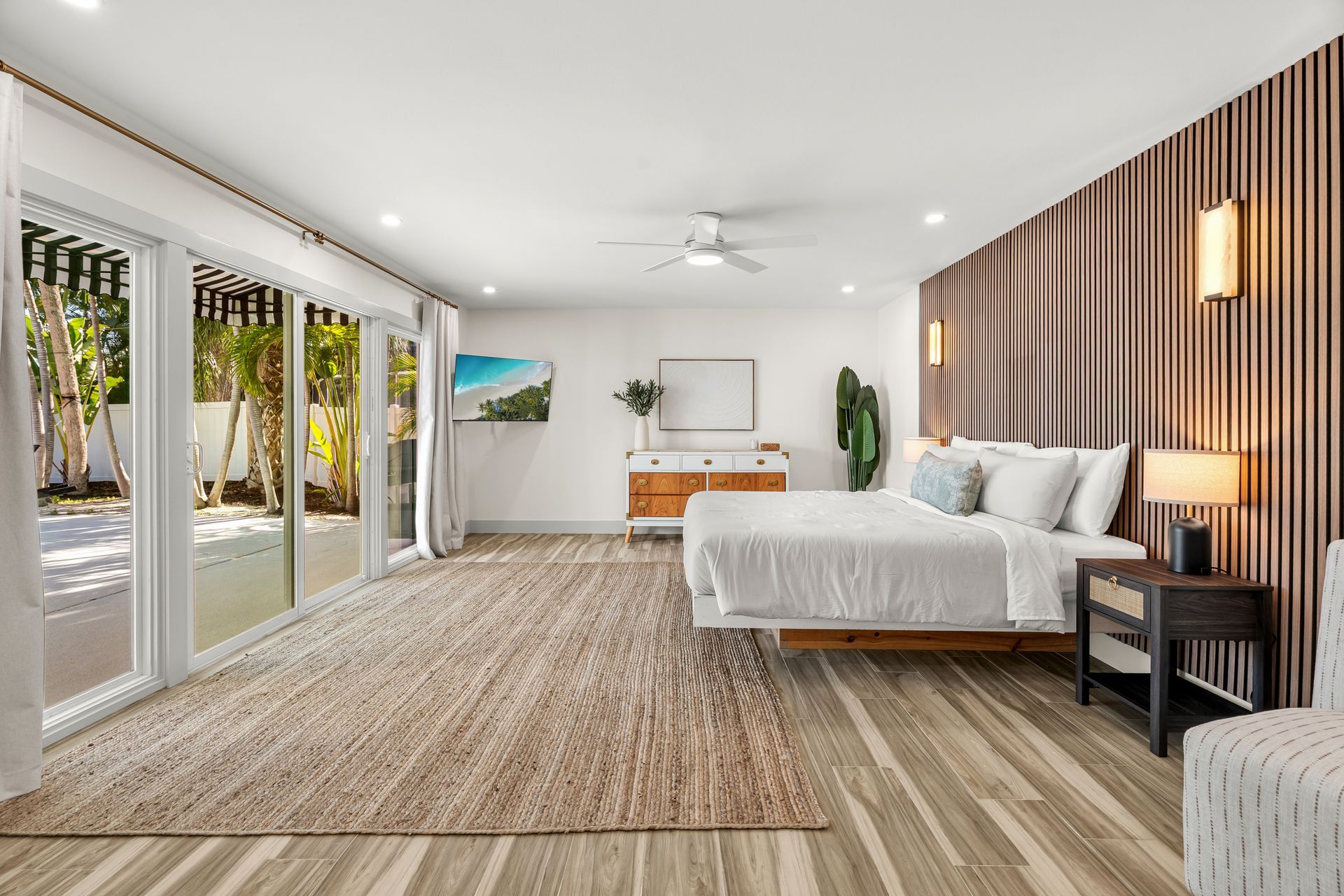 Bright modern bedroom with a king bed, sliding glass doors, striped accent wall, and wood desk.