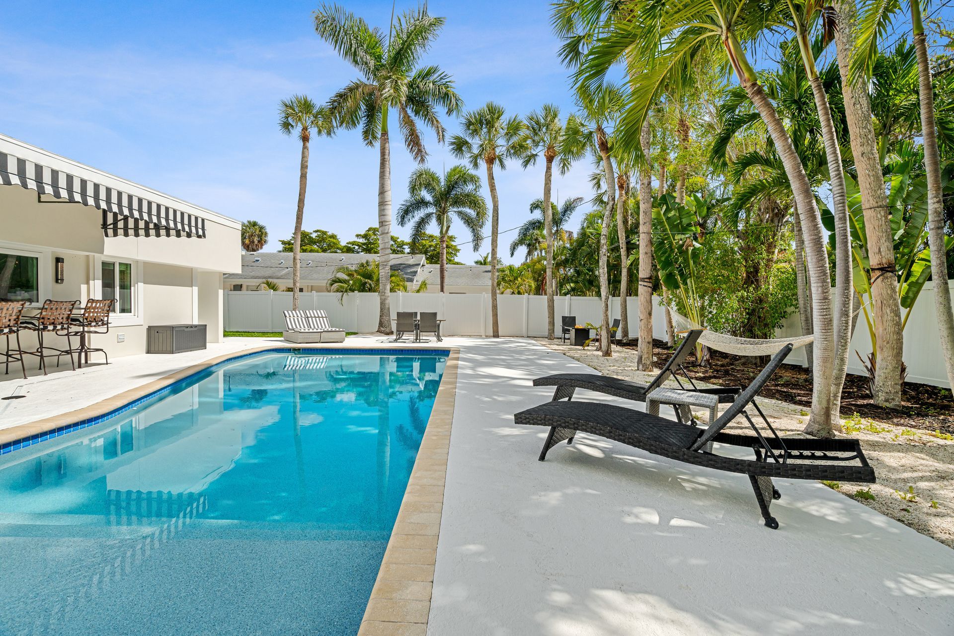 Modern outdoor pool with lounge chairs, palm trees, and a sunny resort patio