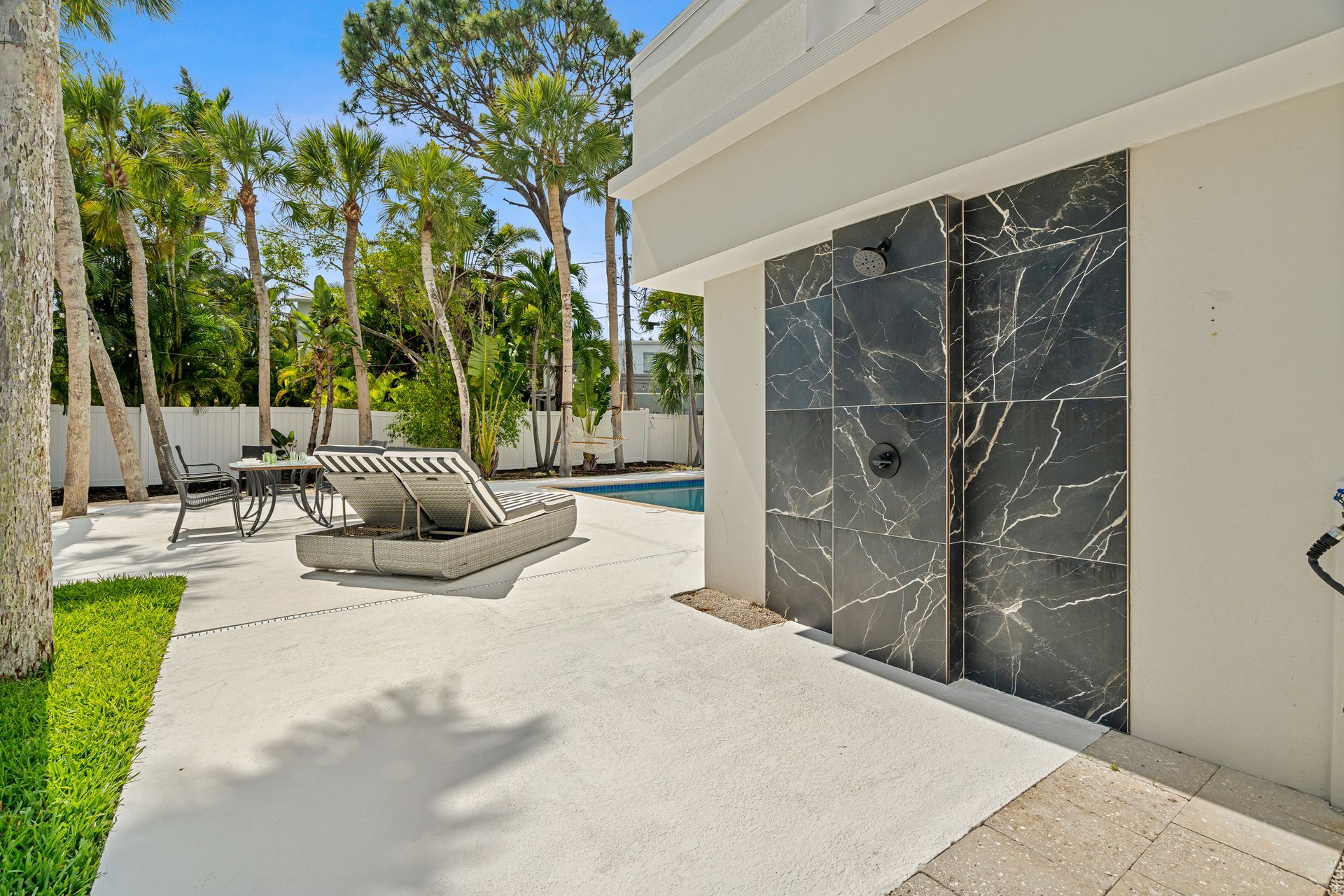 Modern patio with lounge chairs, pool, and tall trees beside a white house