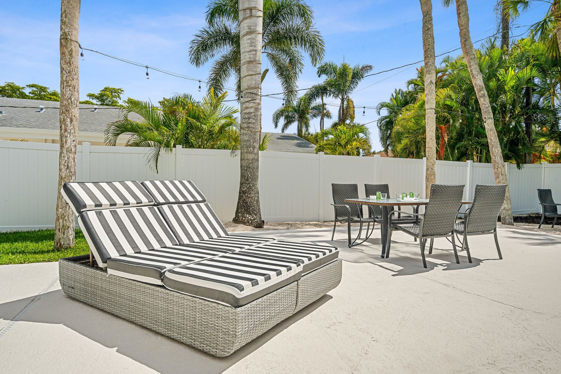 Sunny patio with striped lounge chair, small table and chairs, palm trees, and a white privacy wall