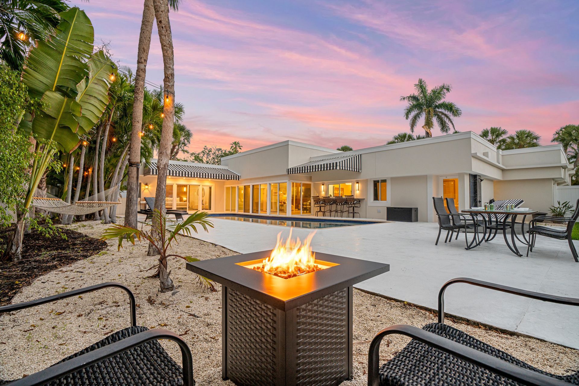 Modern backyard patio at sunset with a fire pit, lounge chairs, and a house glowing in the background