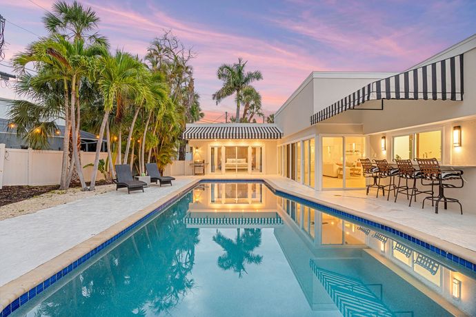 Backyard pool at sunset beside a modern home with palm trees and patio seating