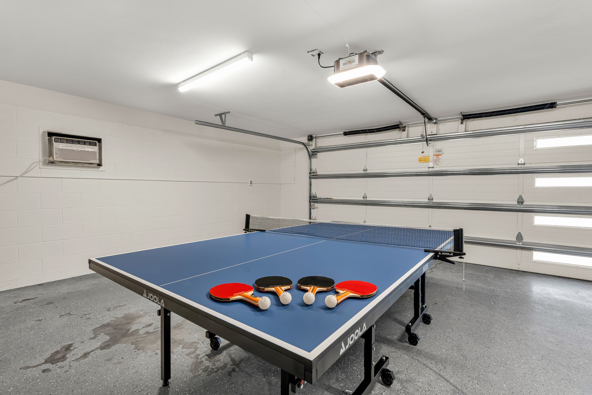 Ping-pong table with paddles in a clean garage, near a white sectional garage door.