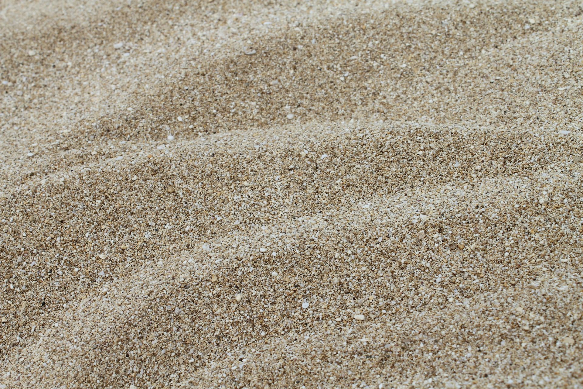 Close-up of beige sand with gentle ripples and speckled texture