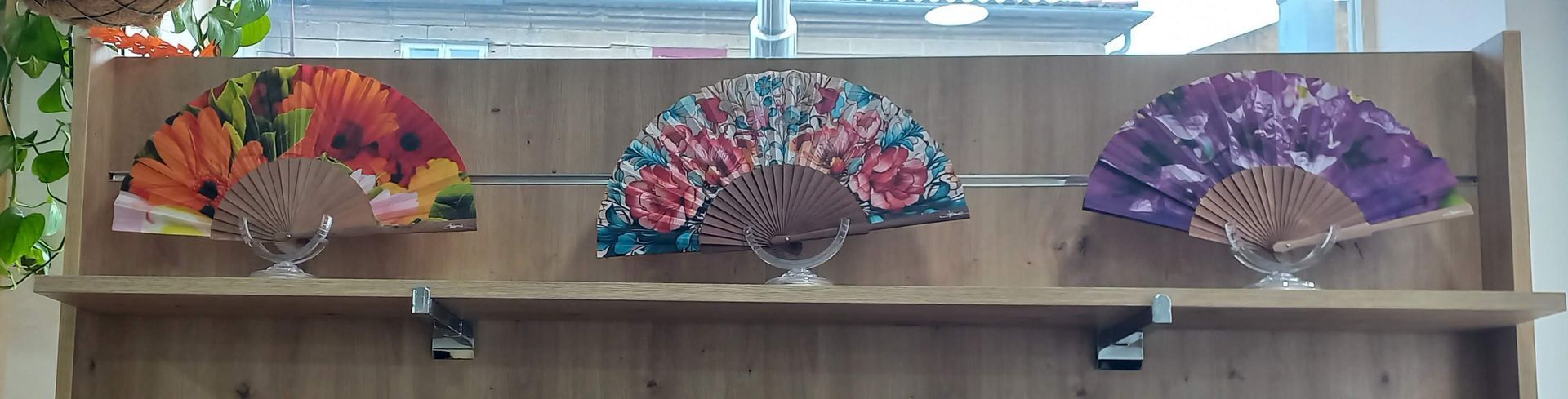 Tres abanicos decorativos con motivos florales expuestos en un estante de madera.