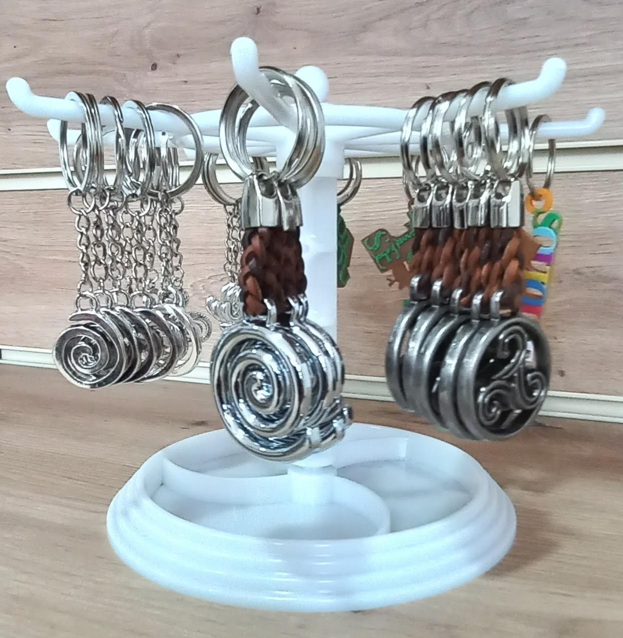 Expositor blanco con llaveros plateados. Algunos tienen colgantes decorativos y cuero trenzado.