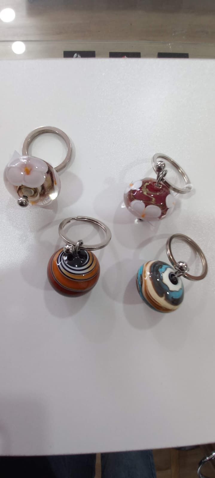 Cuatro dijes de cuentas con anillos de plata. Uno es una flor rosa, otro un corazón rojo y los otros dos son redondos con motivos azules y marrones.