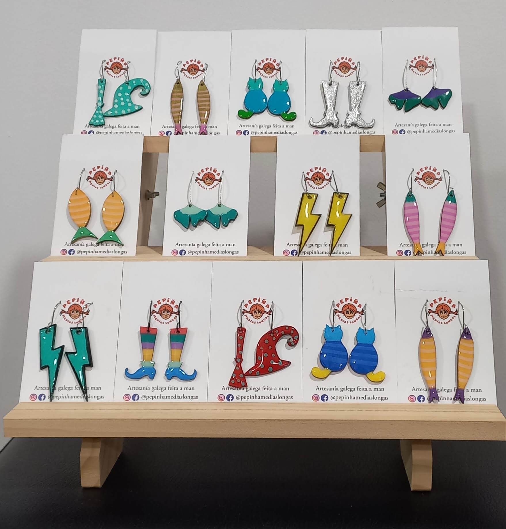 Pendientes expuestos en un soporte de madera. Diversos diseños coloridos y originales sobre cartulinas blancas.