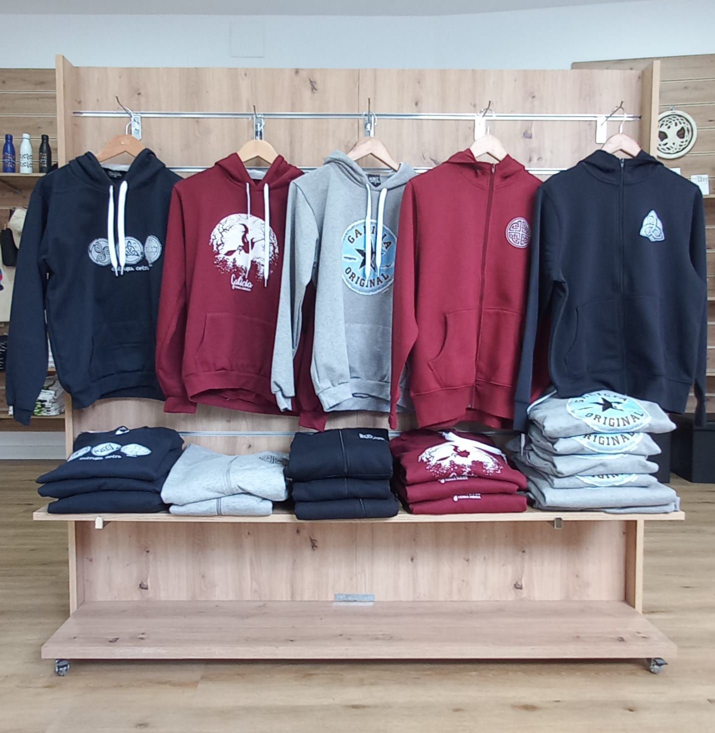 Sudaderas y camisetas en exhibición en una tienda; varios colores, logotipos y diseños.