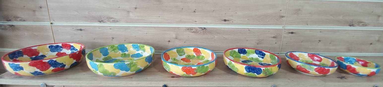 Seis cuencos oblongos, coloridos y estampados, alineados en un estante de madera.