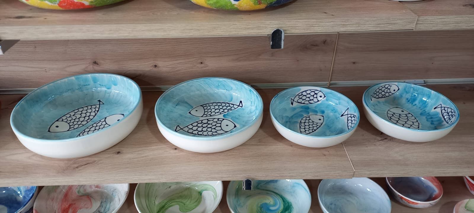 Cuatro cuencos de cerámica con interiores azules decorados con peces sobre un estante de madera.