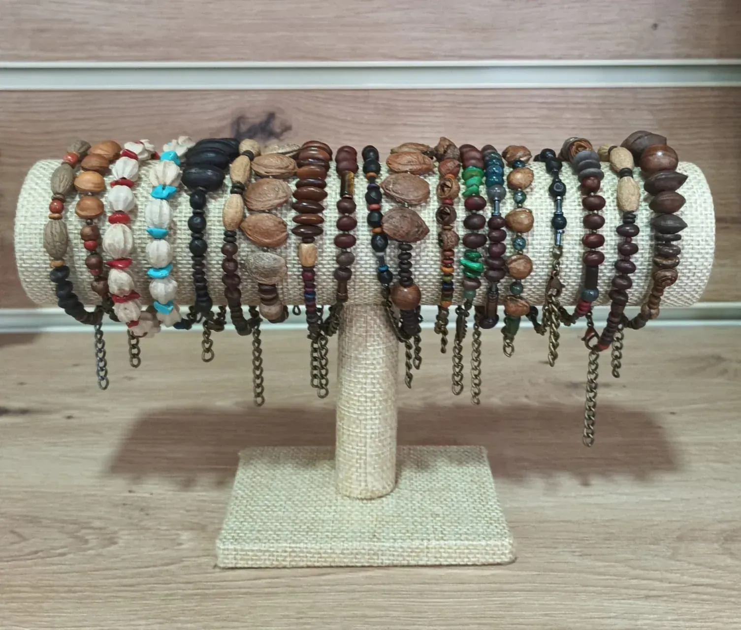Pulseras hechas con cuentas de madera y cadenas exhibidas en un soporte de joyería de color bronce.