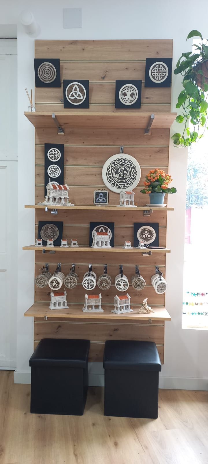 Estantería de madera con diversos objetos decorativos, como obras de arte y tazas. Debajo hay dos otomanas negras.