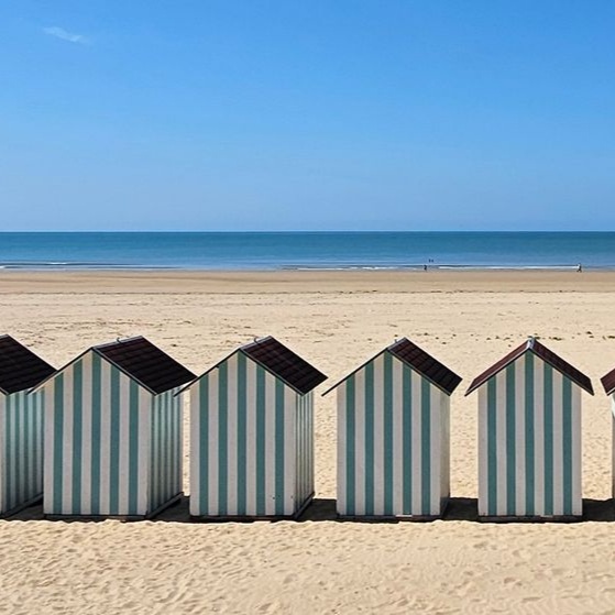 Rangée de cabanes de plage rayées sur une plage de sable, avec l'océan et le ciel bleu en arrière-plan.