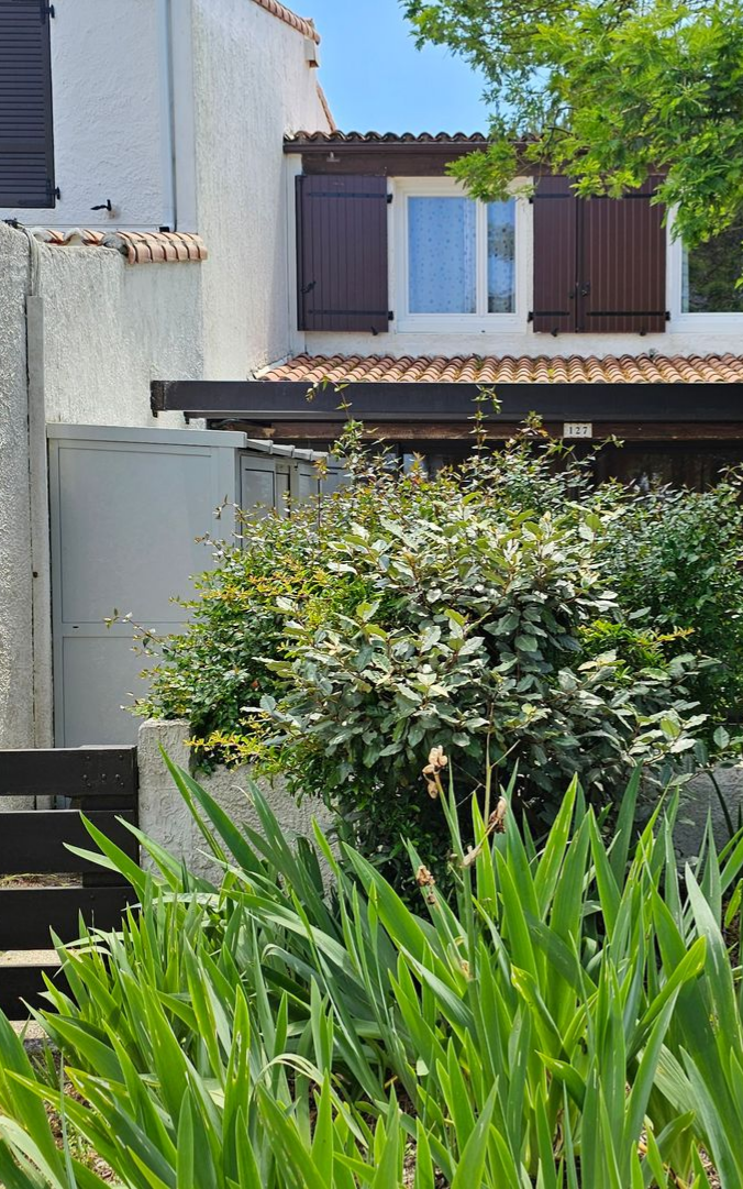 Bâtiment blanc de deux étages avec des volets bruns et un jardin verdoyant luxuriant à l'avant.