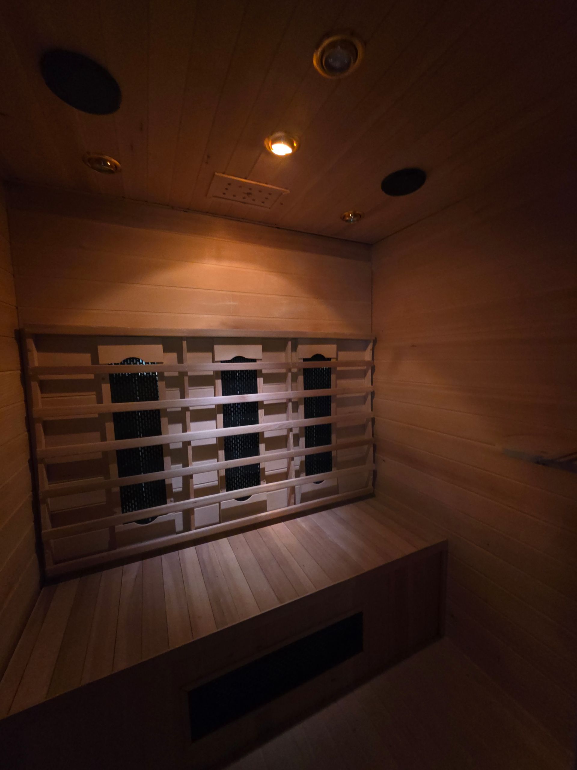 Intérieur de sauna en bois avec bancs, seau et éclairage au plafond.