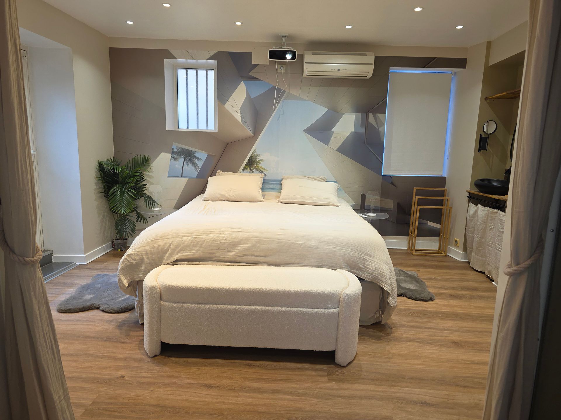 Chambre avec lit, table de chevet, papier peint à motifs et parquet. Fenêtre avec rideaux.