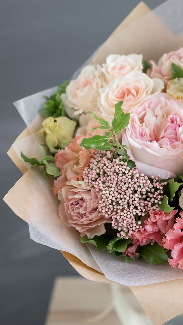 Bouquet de fleurs rose pâle et pêche, emballé dans du papier kraft.