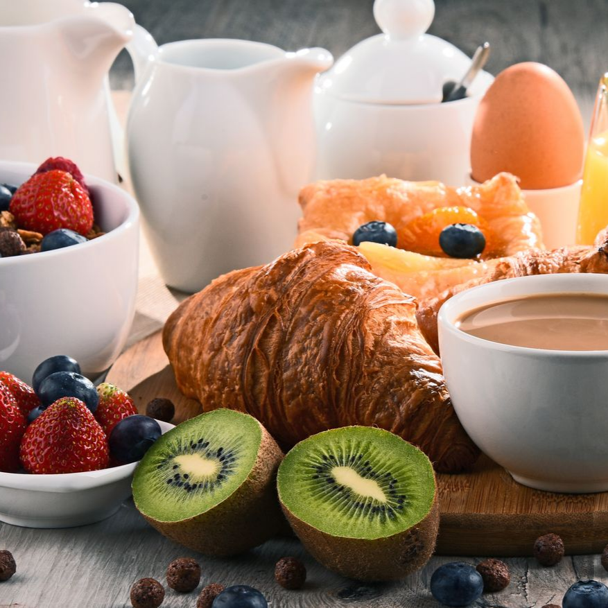 Petit-déjeuner composé d'un croissant, de fruits et de café.