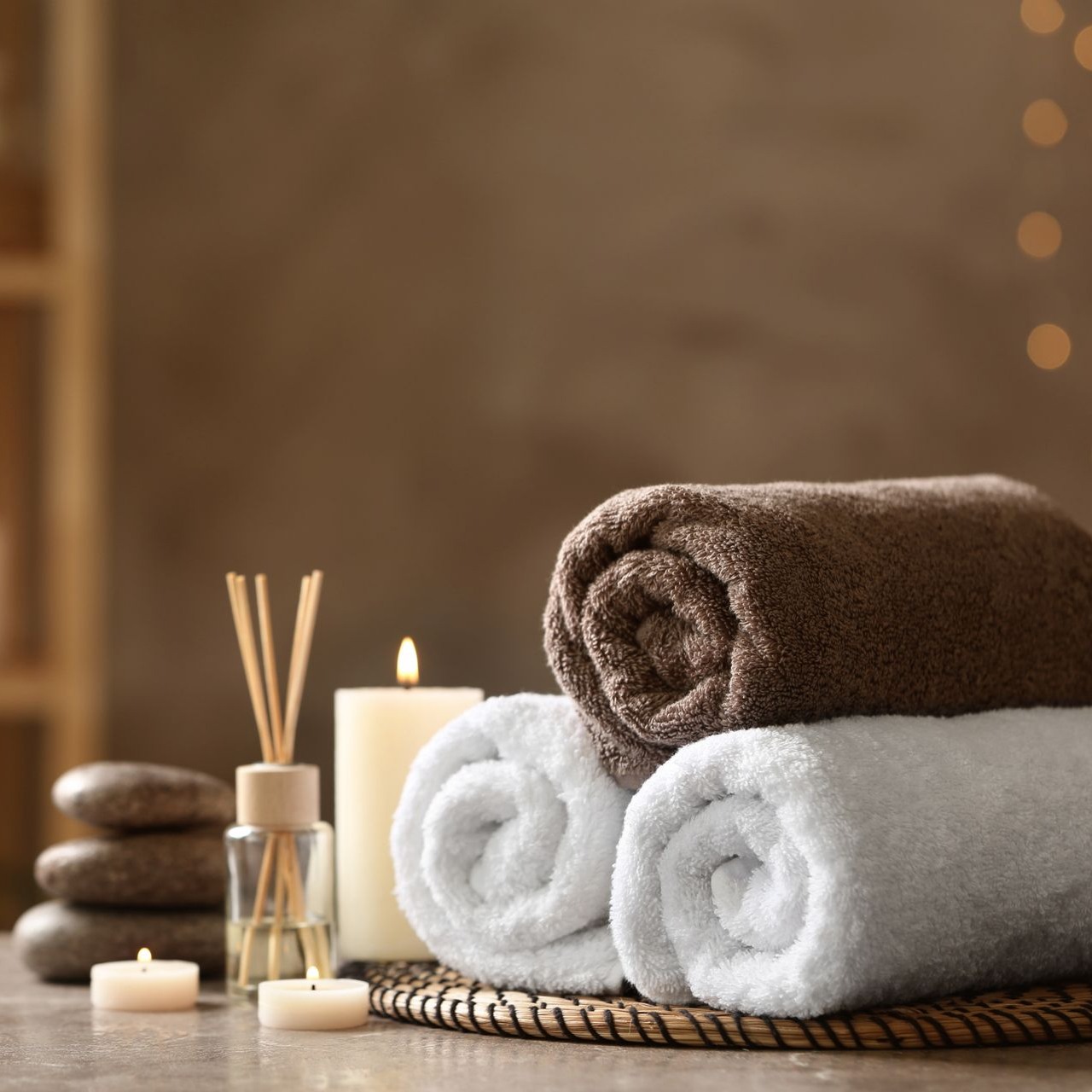 Serviettes roulées dans un décor de spa avec bougies, diffuseur et pierres de massage.
